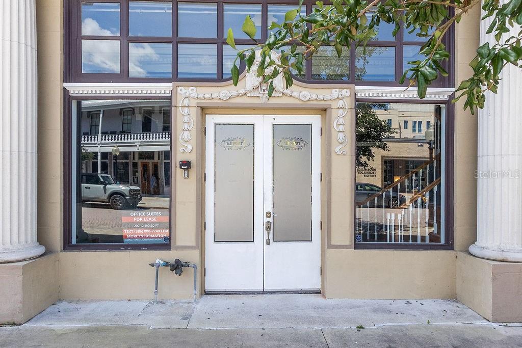 The exterior of a commercial building features double glass doors flanked by large display windows — 112 W INDIANA AVENUE UNIT 206, DELAND, FL
