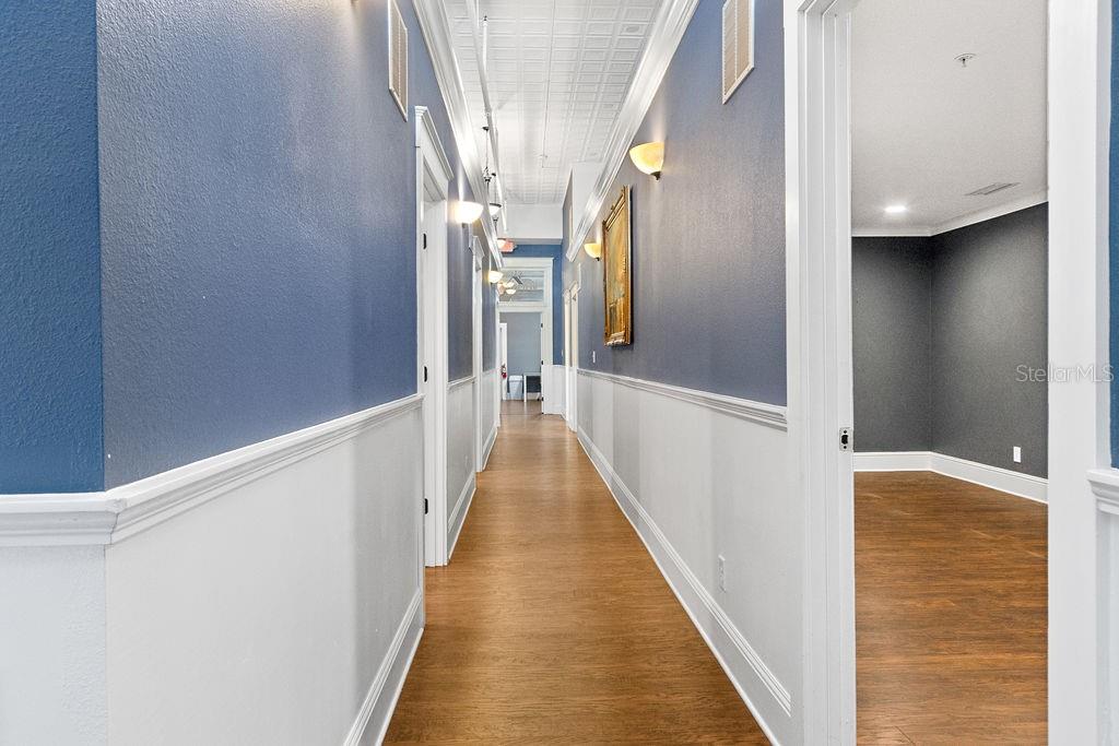 A long hallway with blue walls, white wainscoting, wood flooring, and a decorative tin ceiling — 112 W INDIANA AVENUE UNIT 206, DELAND, FL