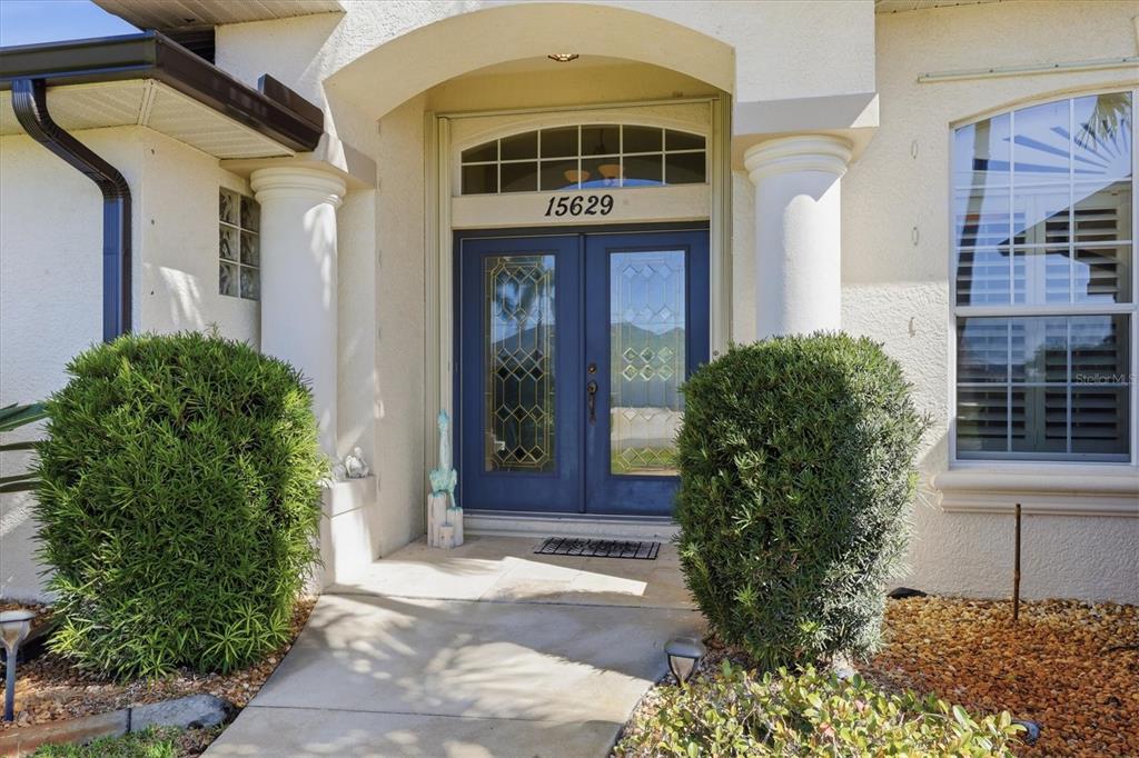 A blue double front door with glass panels sits between two large green bushes — 15629 HAVANA CIRCLE, PORT CHARLOTTE, FL