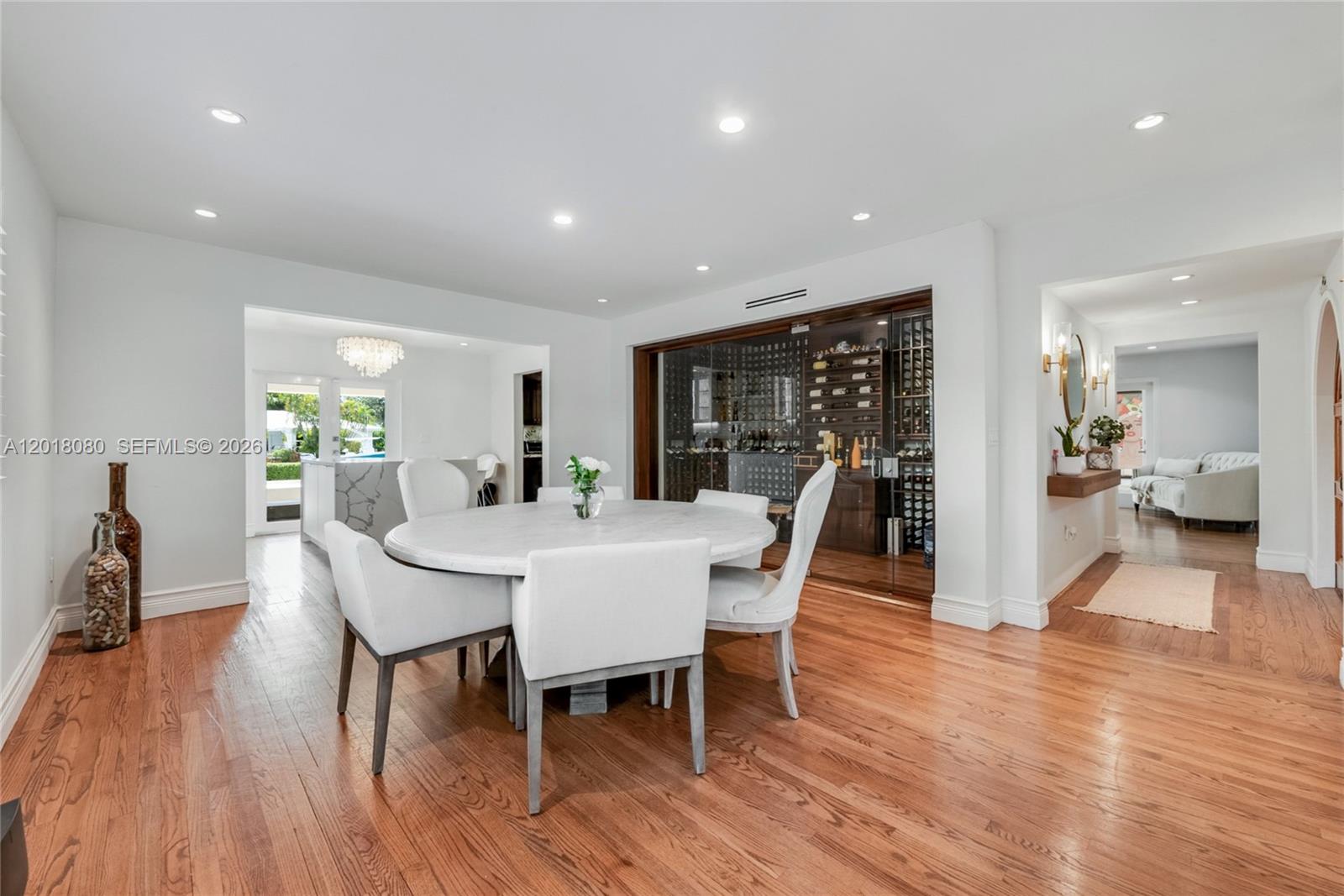 A dining room features a round table, white chairs, hardwood floors, and a glass-enclosed wine cellar — 13035 Nevada St, Coral Gables FL 33156, CORAL GABLES, FL