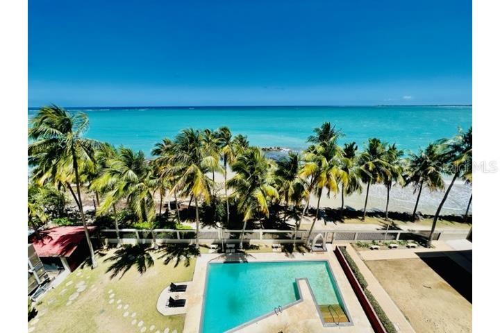 An elevated view of a swimming pool, palm trees, and a beach with turquoise water — 3307 ISLA VERDE AVE. UNIT 1203 A, CAROLINA, PR