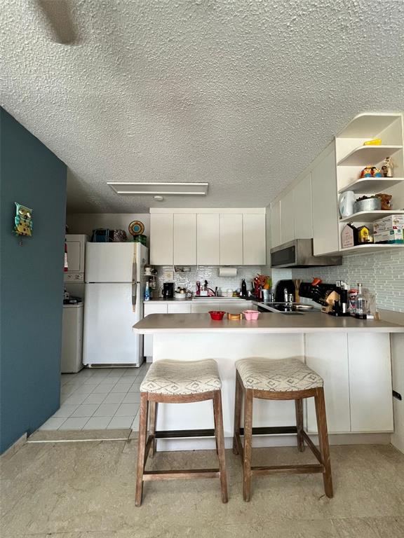 A kitchen features white cabinetry, a breakfast bar with two stools, and a white refrigerator — 3307 ISLA VERDE AVE. UNIT 1203 A, CAROLINA, PR