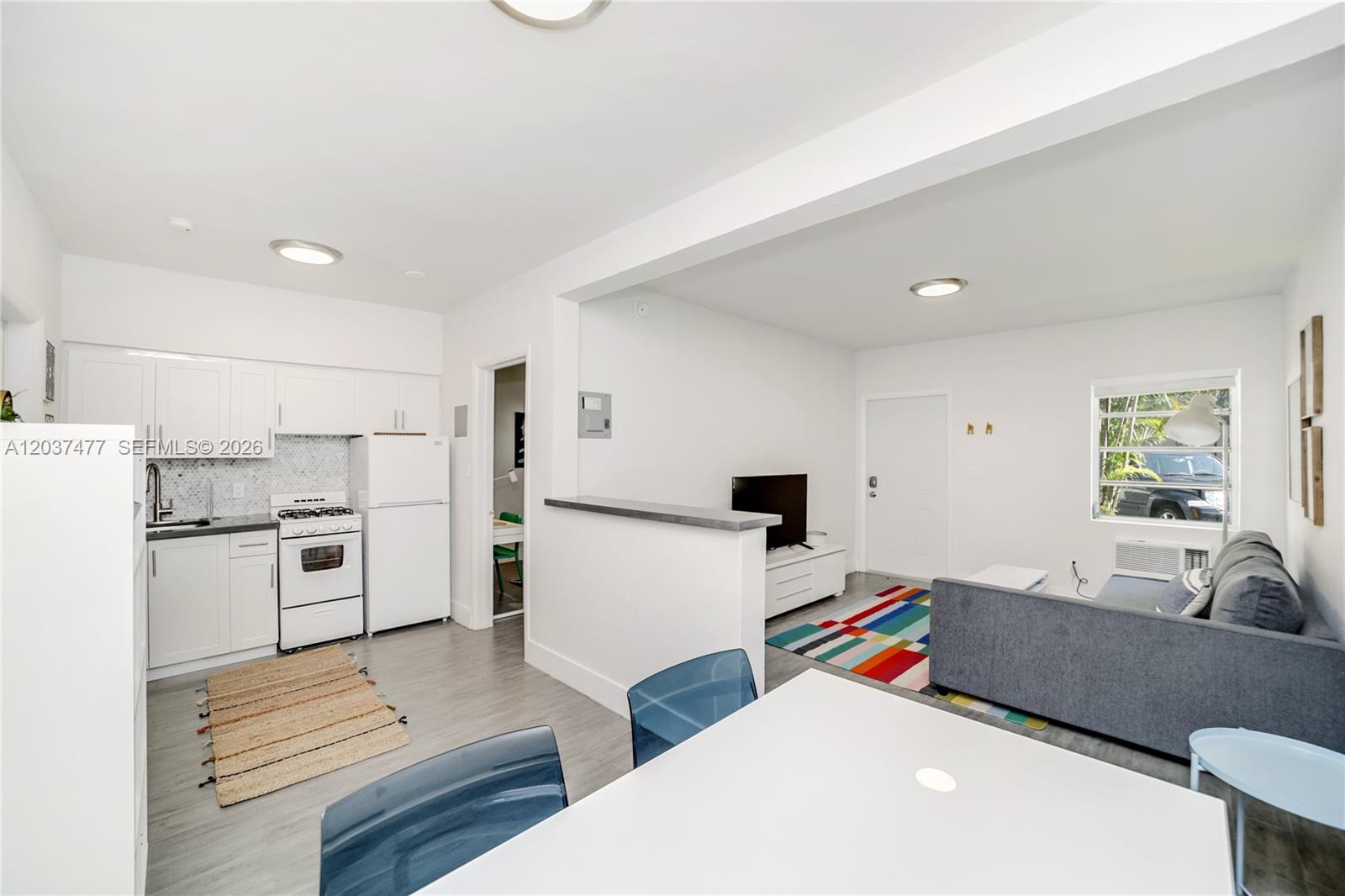 A bright, open-concept living area features a white kitchen, dining space, and a gray sofa — 770 NE 123rd St # 24, North Miami FL 33161, NORTH MIAMI, FL