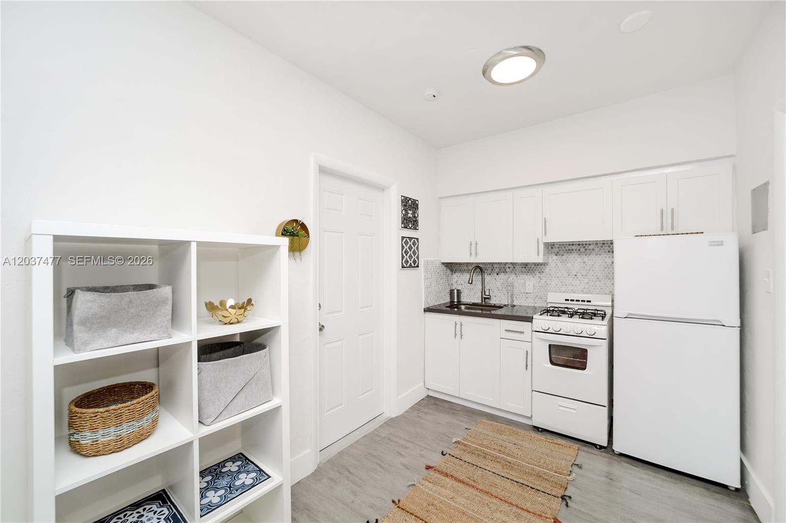A small kitchen features white cabinets, a gas stove, a refrigerator, and a shelving unit — 770 NE 123rd St # 24, North Miami FL 33161, NORTH MIAMI, FL