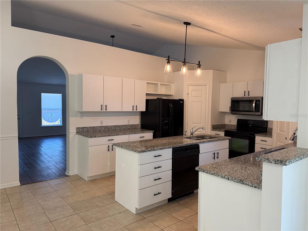 A kitchen features white cabinets, granite countertops, a black refrigerator, and a central island — 916 NANCY COURT, KISSIMMEE, FL