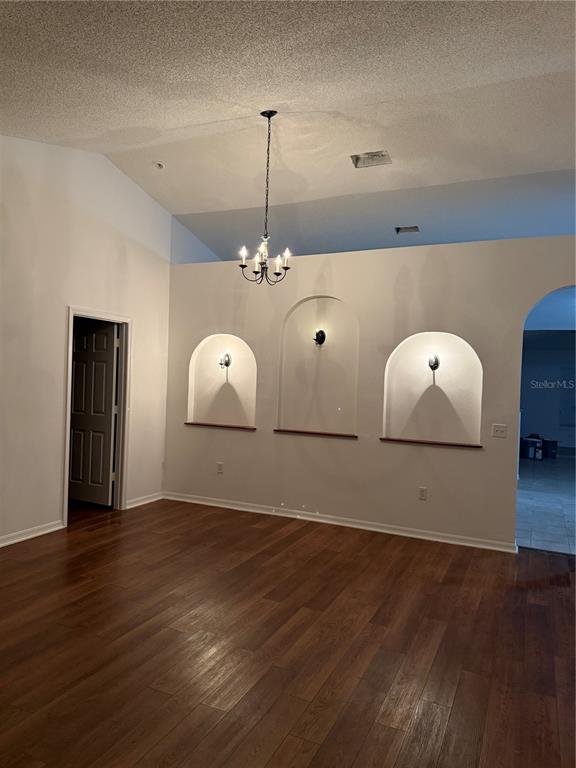An empty living room features dark wood-look flooring, white walls, and three arched wall niches — 916 NANCY COURT, KISSIMMEE, FL