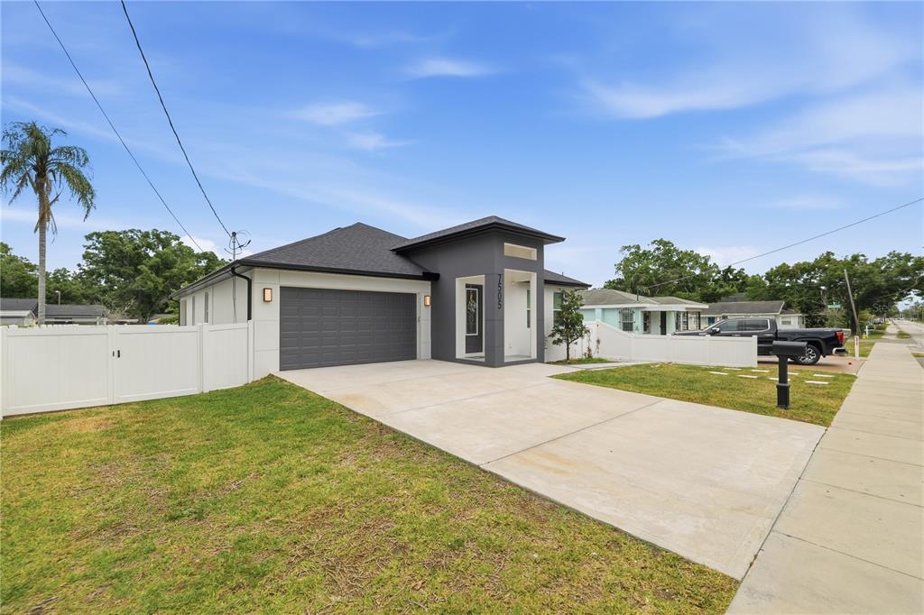 A modern single-story house with a gray exterior, a two-car garage, and a white fence — 7505 N ROME AVENUE, TAMPA, FL