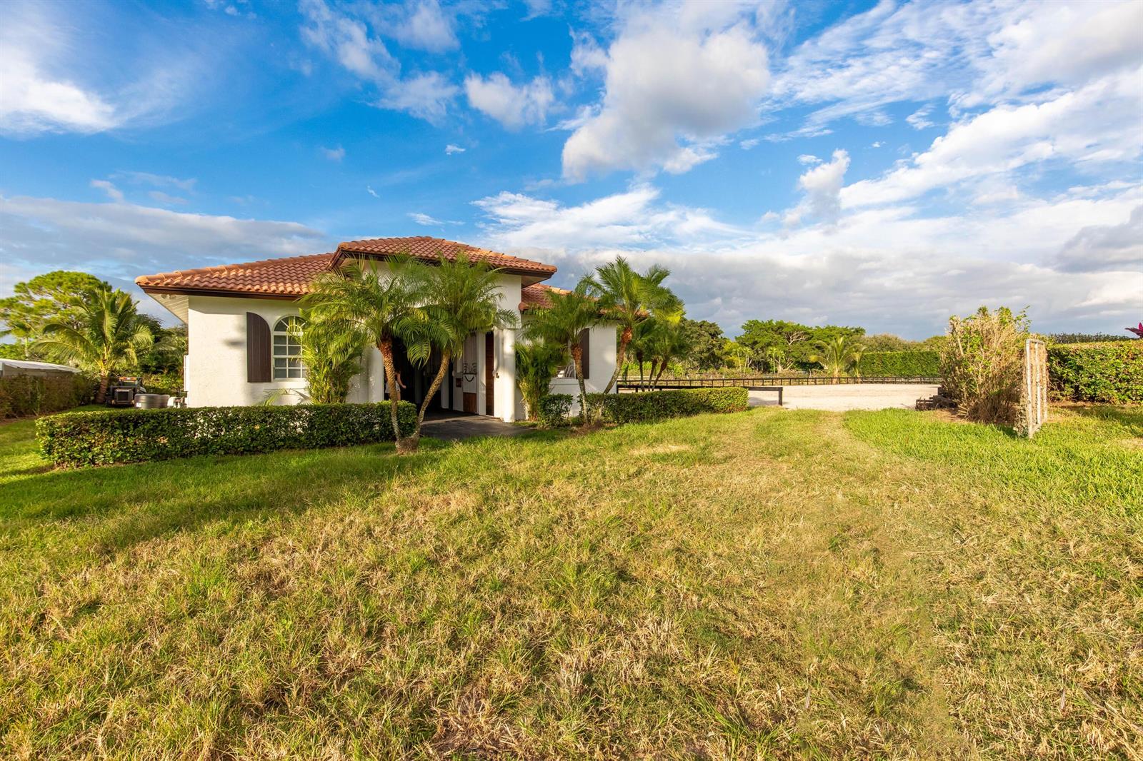 A white, single-story house with a tile roof sits on a grassy lot with palms — 14367 Belmont Trace, Wellington FL 33414, WELLINGTON, FL