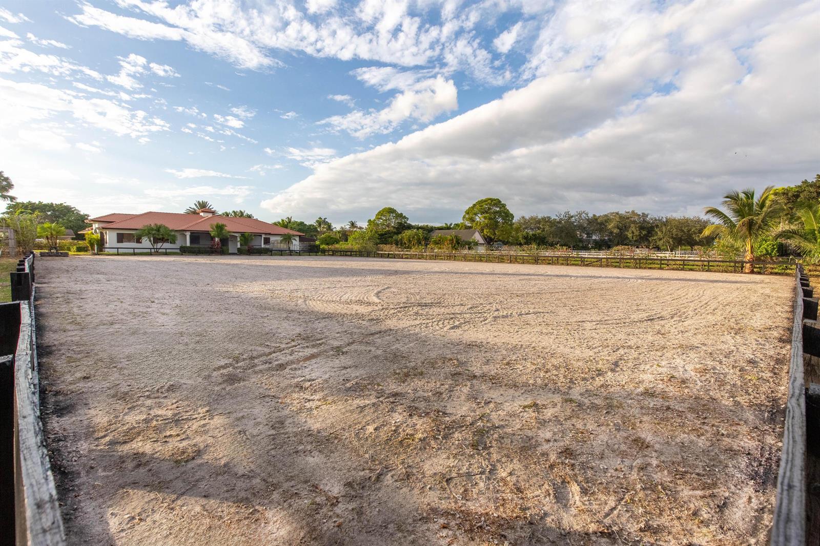 A large, fenced-in sandy horse riding arena sits in front of a residential house — 14367 Belmont Trace, Wellington FL 33414, WELLINGTON, FL