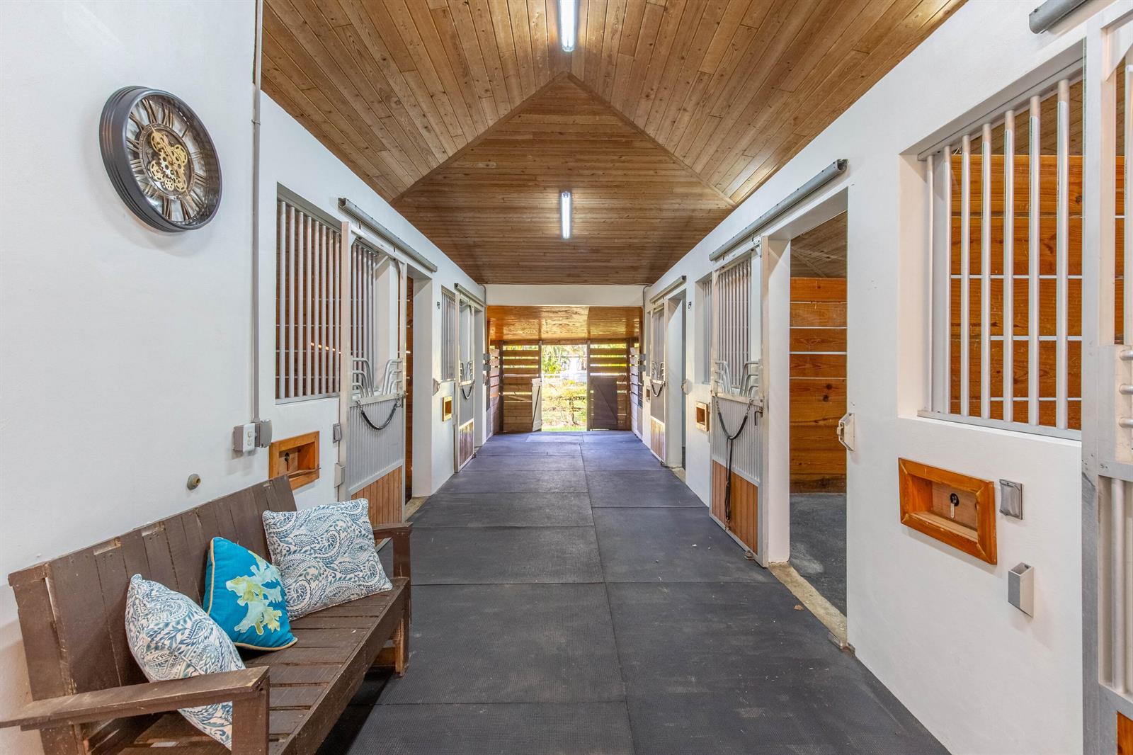A horse stable aisle features a wooden vaulted ceiling, rubber flooring, and several stall doors — 14367 Belmont Trace, Wellington FL 33414, WELLINGTON, FL