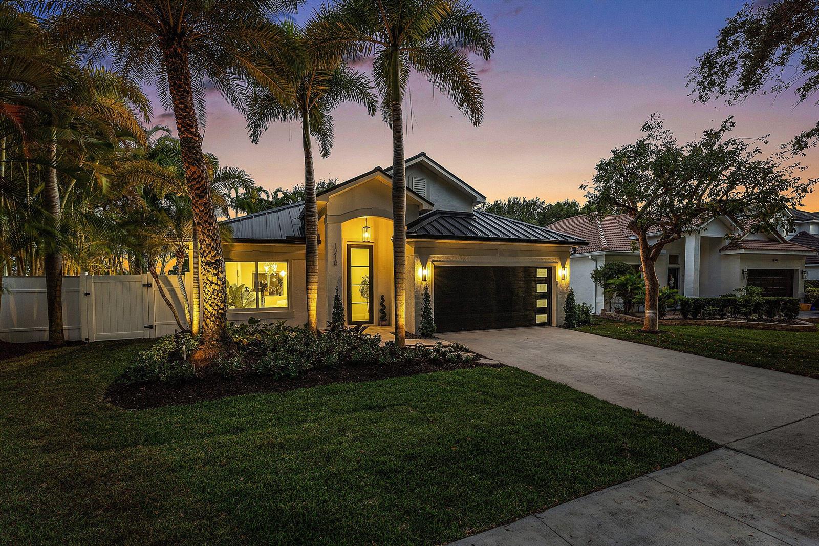 A single-story house with a dark metal roof, palm trees, and a concrete driveway at dusk — 1210 Delray Lakes Drive, Delray Beach FL 33444, DELRAY BEACH, FL