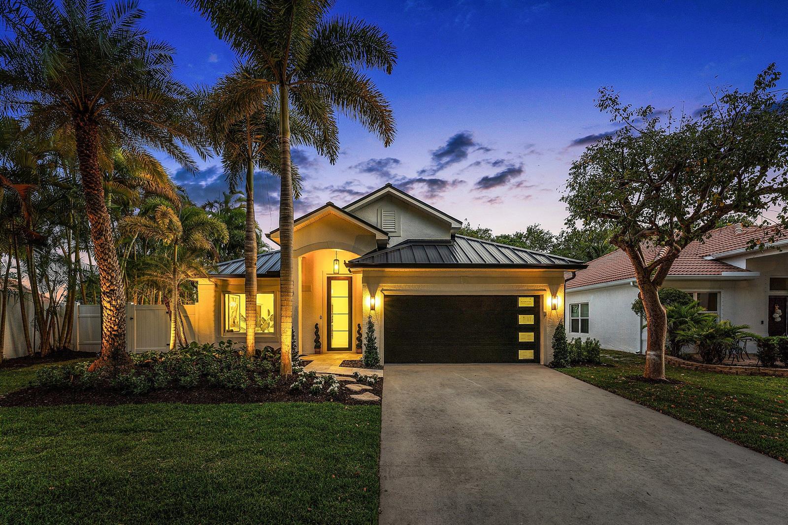 A single-story house with a dark metal roof, palm trees, and a concrete driveway at dusk — 1210 Delray Lakes Drive, Delray Beach FL 33444, DELRAY BEACH, FL