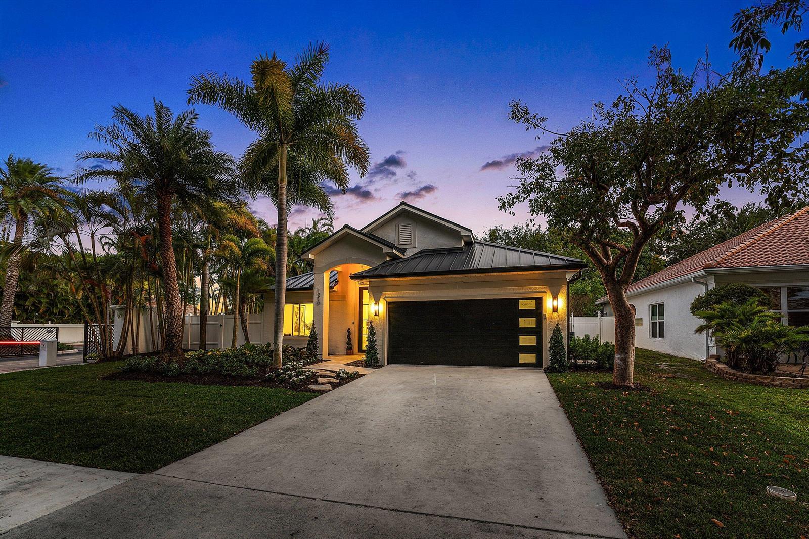 A single-story house with a dark metal roof, black garage door, and palm trees at dusk — 1210 Delray Lakes Drive, Delray Beach FL 33444, DELRAY BEACH, FL