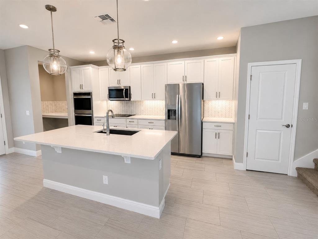 A modern kitchen features white cabinetry, stainless steel appliances, a large island, and light-colored flooring — 7248 CARRICKBEND LANE, ORLANDO, FL