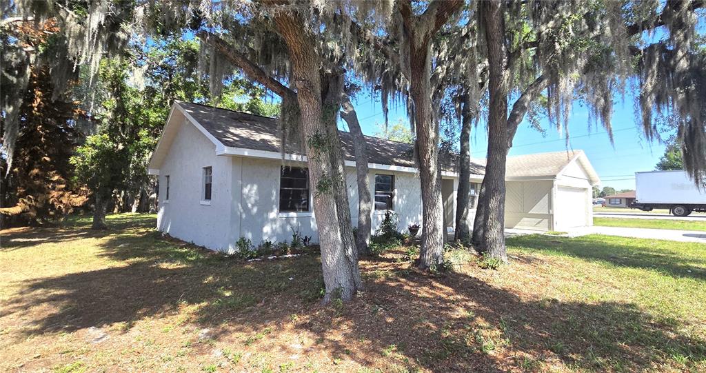 A single-story house with white stucco siding is surrounded by large trees with Spanish moss — 4201 SHADOW WOOD DRIVE, WINTER HAVEN, FL