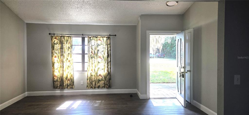 A living room features gray walls, dark wood-look flooring, a window with curtains, and an open door — 4201 SHADOW WOOD DRIVE, WINTER HAVEN, FL