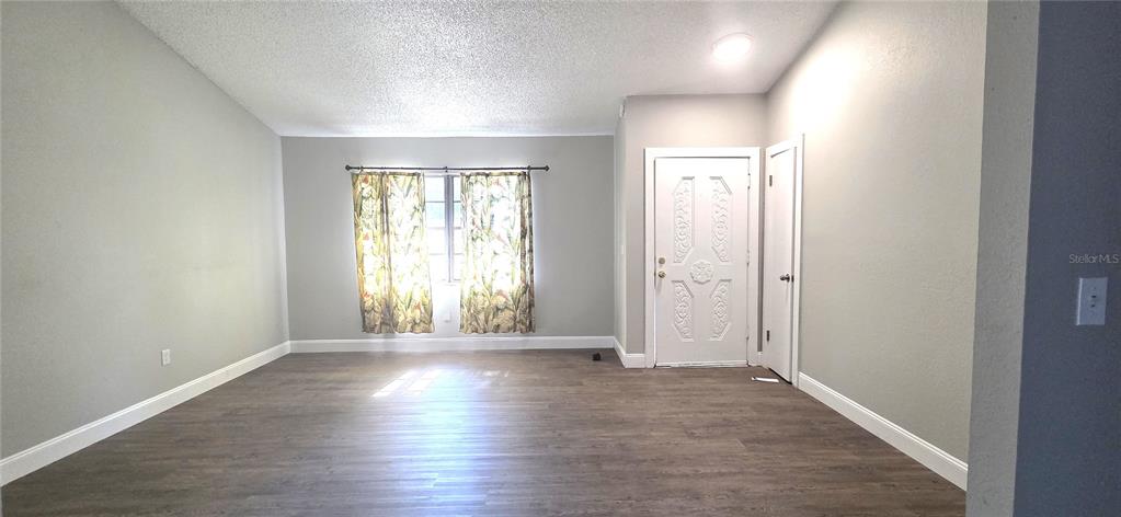 A living room with light gray walls, wood-look flooring, a white front door, and curtains — 4201 SHADOW WOOD DRIVE, WINTER HAVEN, FL