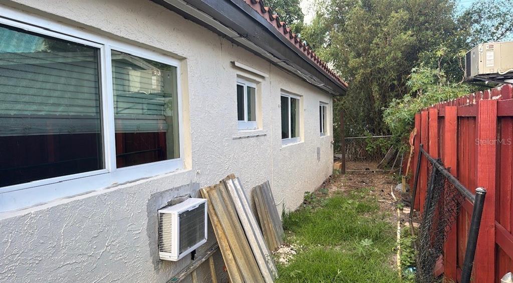 The exterior side of a stucco house features several windows, a wall-mounted air conditioner, and fencing — 490 NW 29TH AVENUE, FORT LAUDERDALE, FL