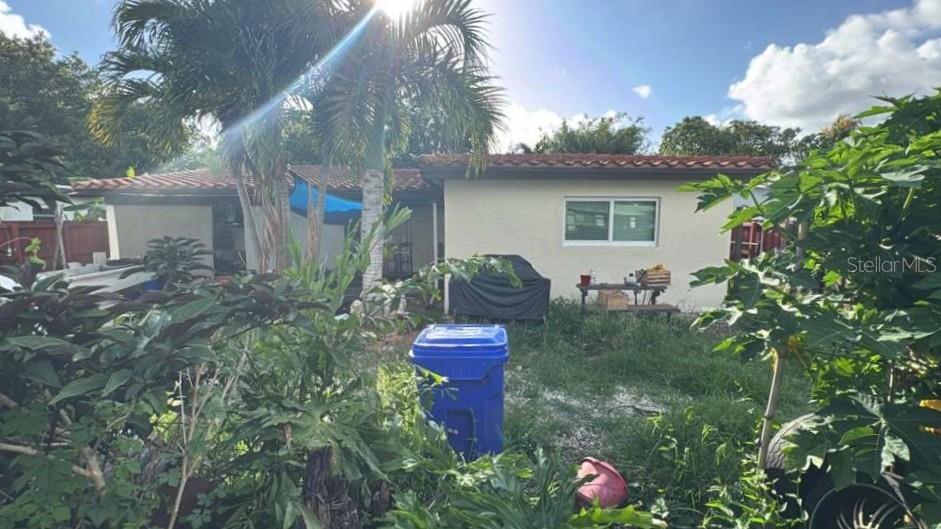 A backyard view of a single-story house with a blue trash bin and palm trees — 490 NW 29TH AVENUE, FORT LAUDERDALE, FL