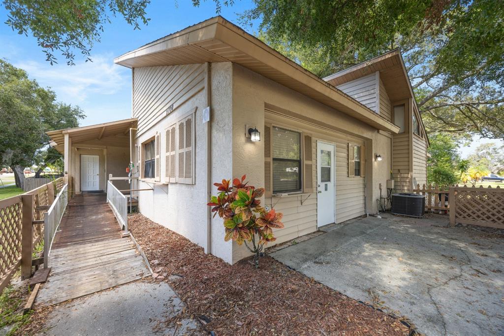 A side view of a house featuring a wooden wheelchair ramp and a concrete patio — 2700 STATE ROAD 590, CLEARWATER, FL
