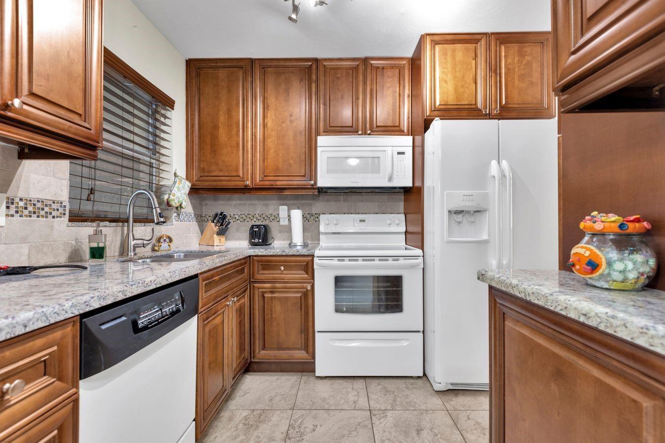 A kitchen with wood cabinets, white appliances, granite countertops, and a tiled backsplash — 6850 Royal Palm Boulevard # 106, Margate FL 33063, MARGATE, FL