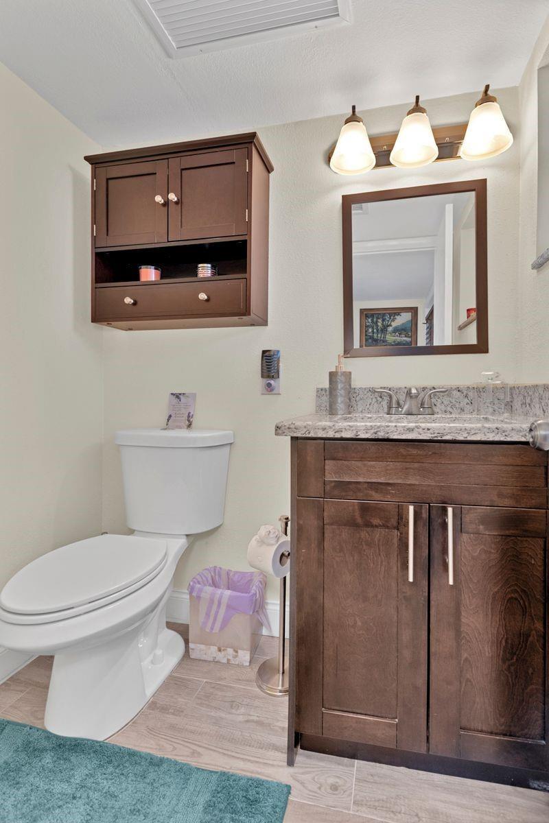 A bathroom features a dark wood vanity with a granite countertop, toilet, and wall-mounted cabinet — 6850 Royal Palm Boulevard # 106, Margate FL 33063, MARGATE, FL