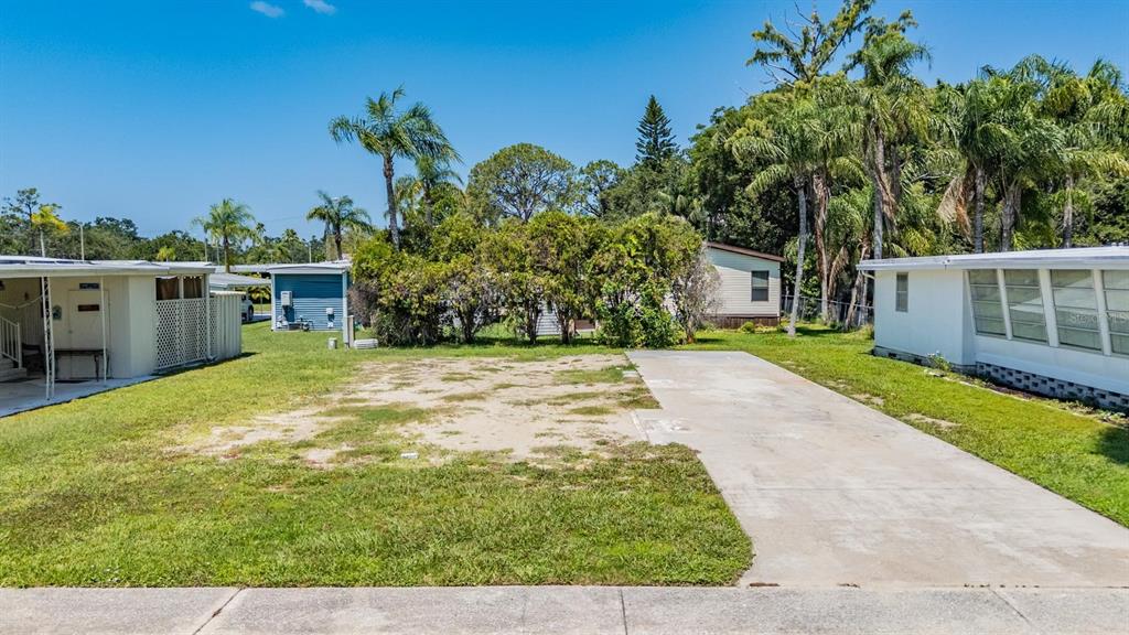An empty residential lot features a concrete driveway between two mobile homes under a clear sky — 605 MICHIGAN BOULEVARD UNIT 105, DUNEDIN, FL