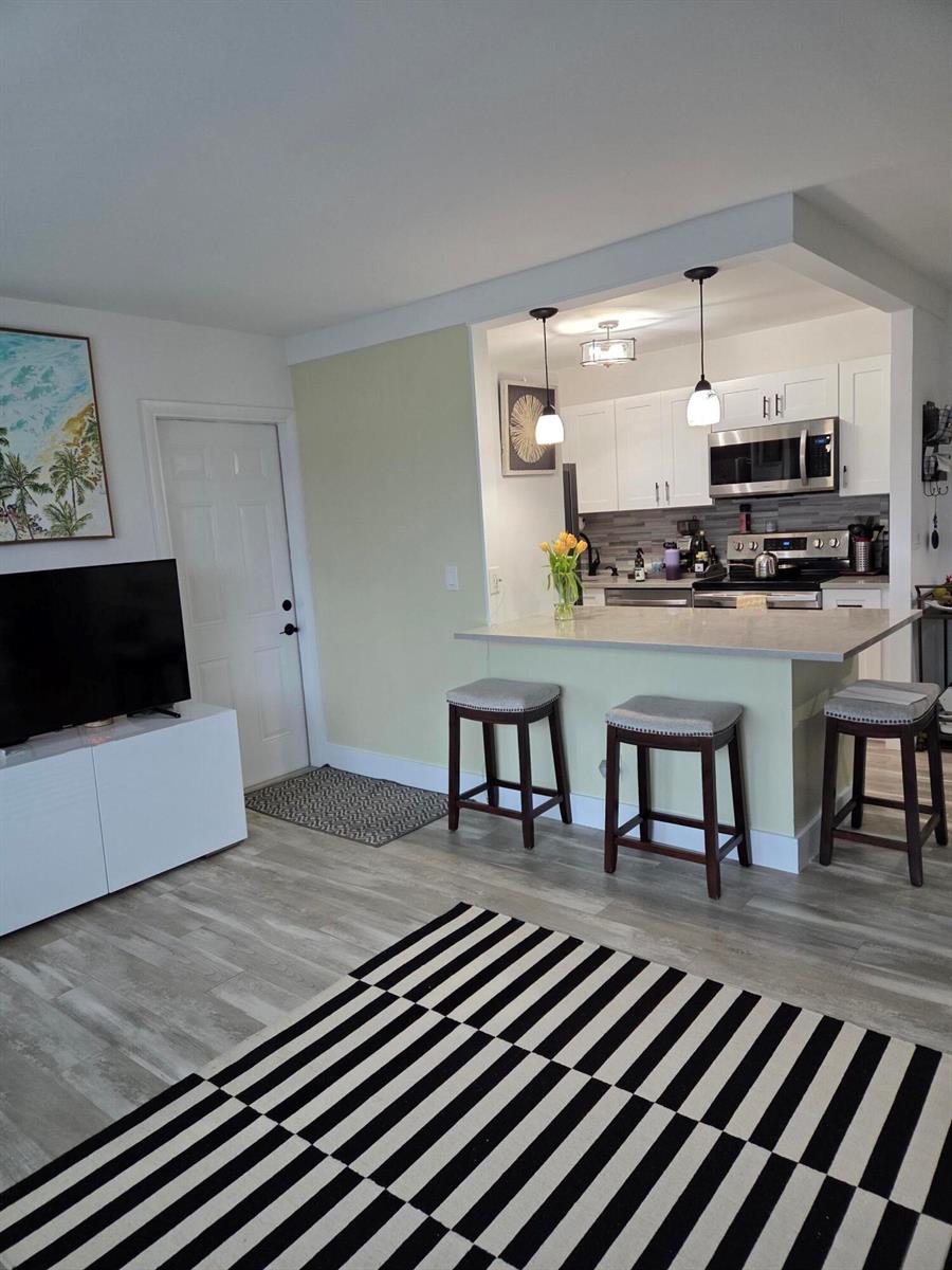 A living room with a striped rug opens to a kitchen featuring a breakfast bar — BOYNTON BEACH, FL