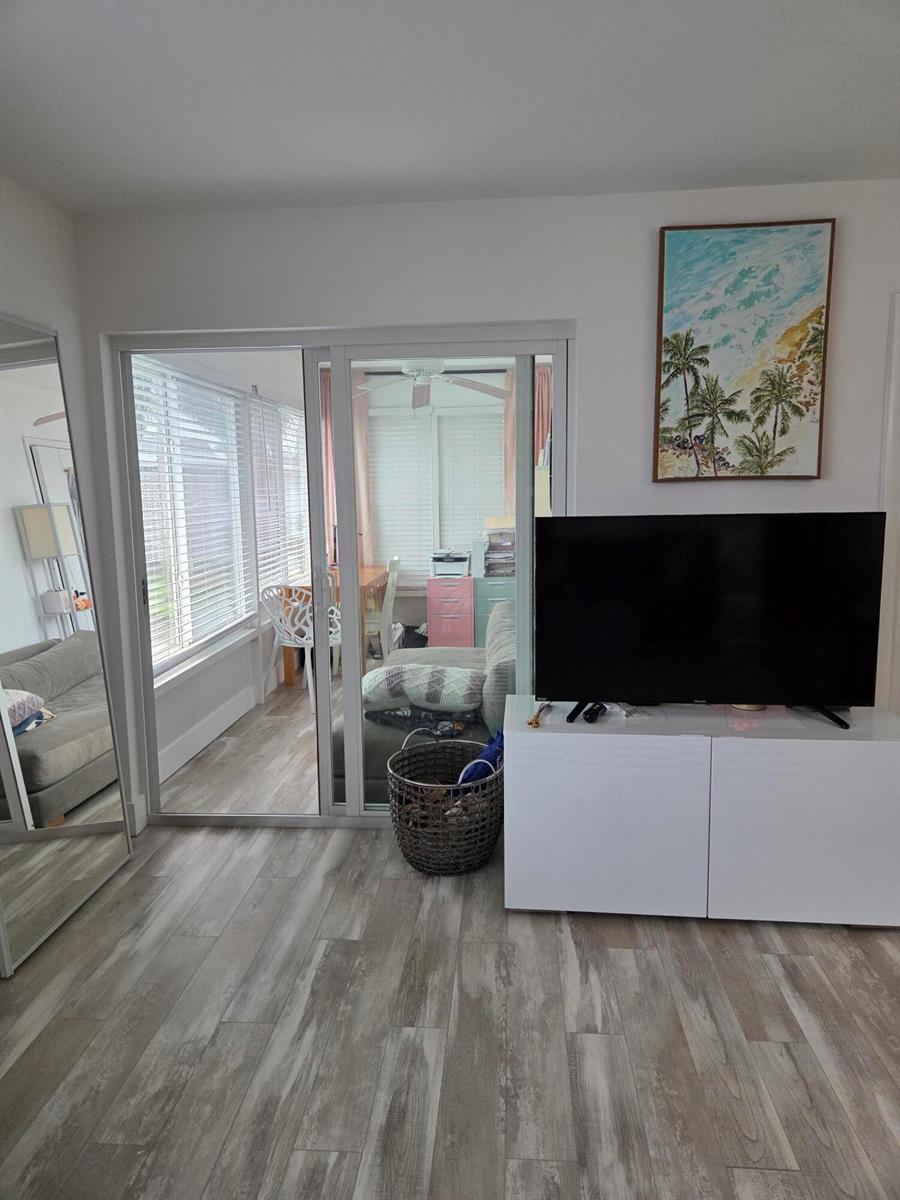 A living room features a white media console, a large television, and sliding glass doors — BOYNTON BEACH, FL