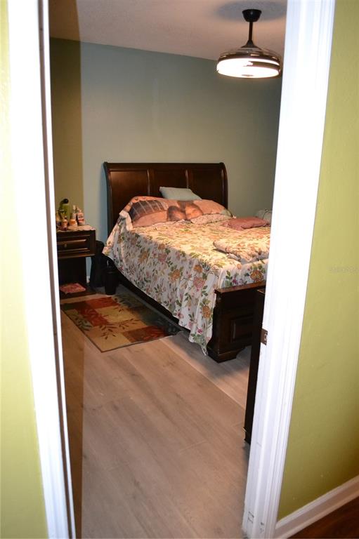 A bedroom with light wood-look flooring, a dark wood bed frame, and a ceiling fan — 509 MARICOPA DRIVE, KISSIMMEE, FL