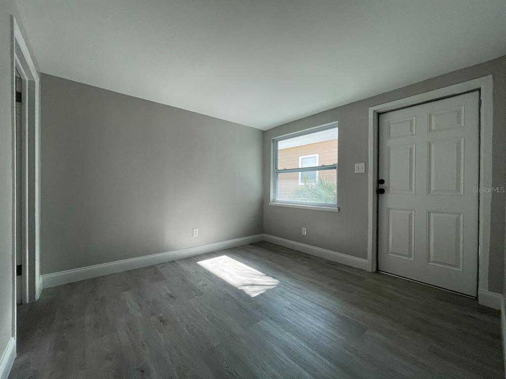 An empty room features gray walls, light wood-look flooring, a window, and a white door — 2704 E COLUMBUS DRIVE UNIT A, TAMPA, FL