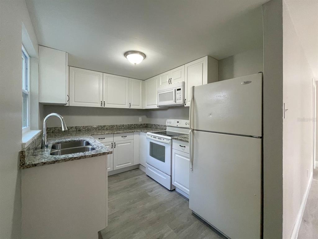 A kitchen features white cabinets, granite countertops, a white refrigerator, and light wood-look flooring — 2704 E COLUMBUS DRIVE UNIT A, TAMPA, FL
