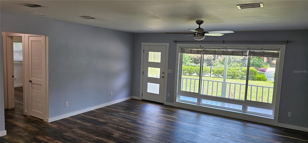 A living room with light blue walls, wood-look flooring, a ceiling fan, and a front door — 2462 HARVARD ROAD, DELAND, FL