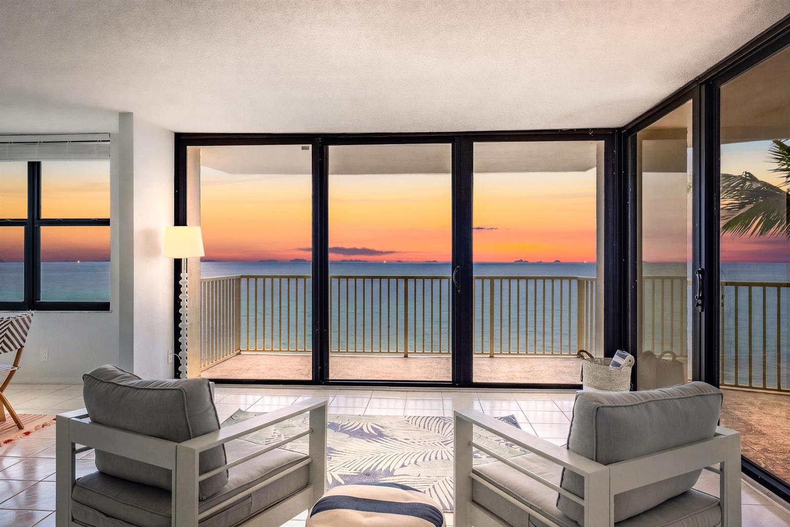 A living room with two chairs faces a balcony overlooking the ocean at sunset — 5480 N Ocean Drive, Singer Island FL 33404, SINGER ISLAND, FL