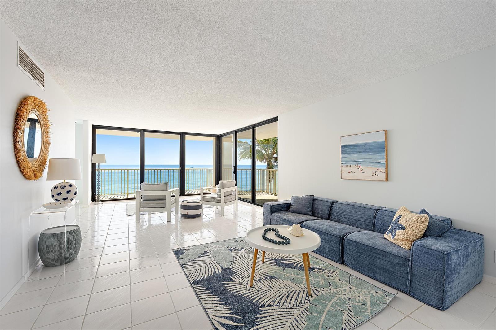 A bright living room features white tile floors, a blue sectional sofa, and ocean views — 5480 N Ocean Drive, Singer Island FL 33404, SINGER ISLAND, FL