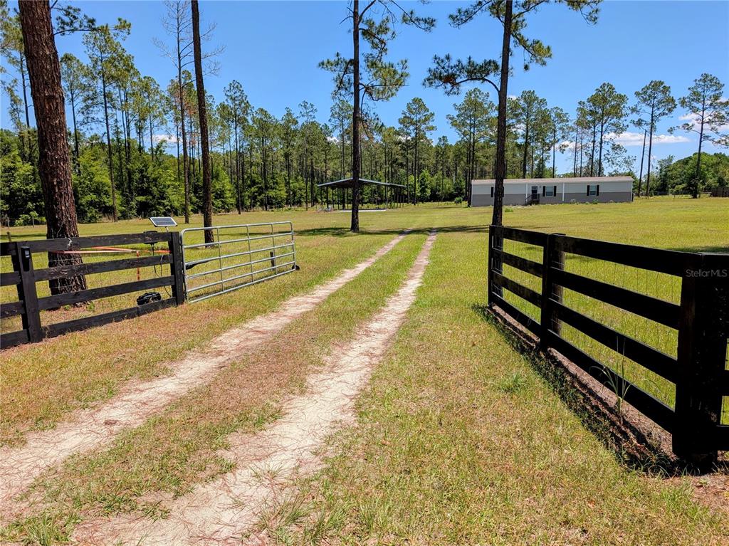 A metal gate opens to a grassy path leading toward a barn on a rural property — 14421 NW 214TH TERRACE, HIGH SPRINGS, FL