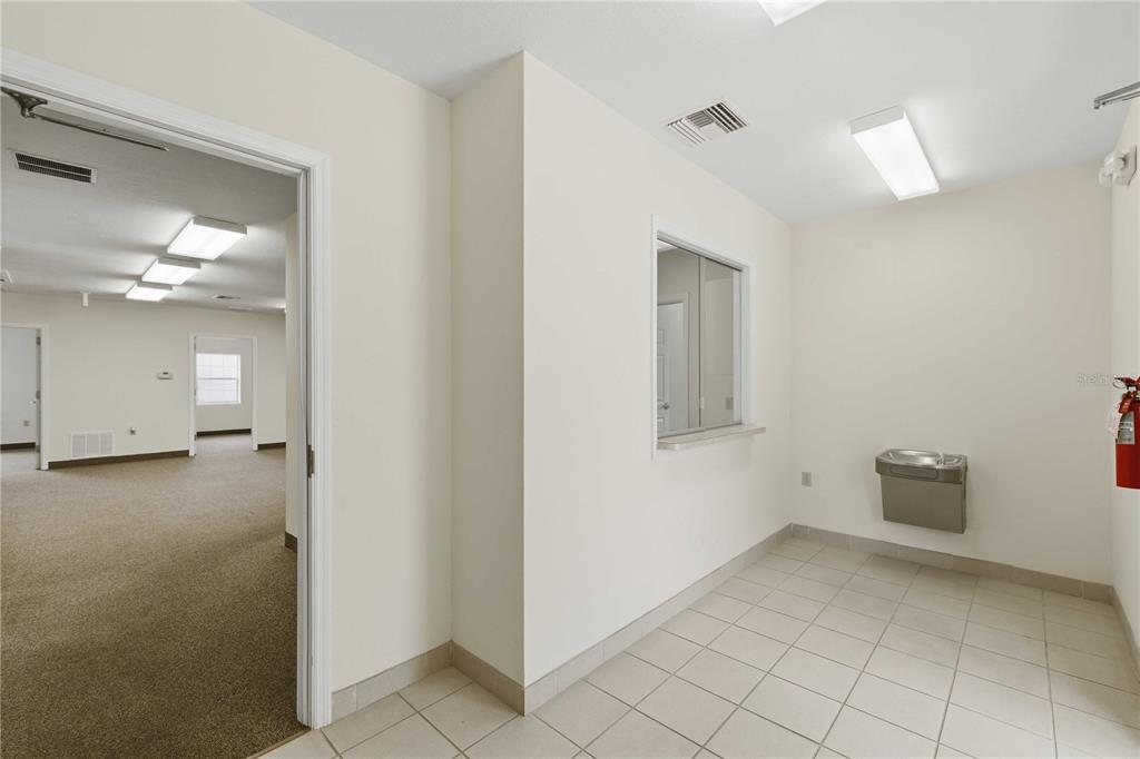 A tiled hallway features a water fountain, a service window, and a doorway to carpeted rooms — 4370 NE 35TH STREET UNIT 3, OCALA, FL