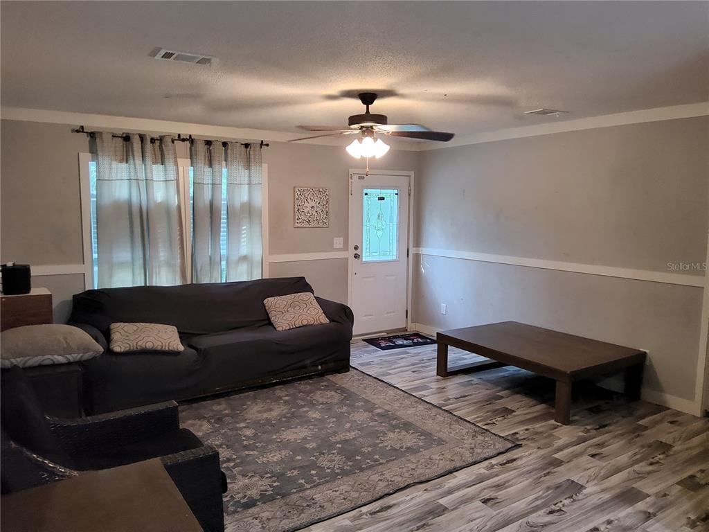 A living room features gray walls, wood-look flooring, a dark sofa, and a ceiling fan — 3200 SE 107TH PLACE, OCALA, FL