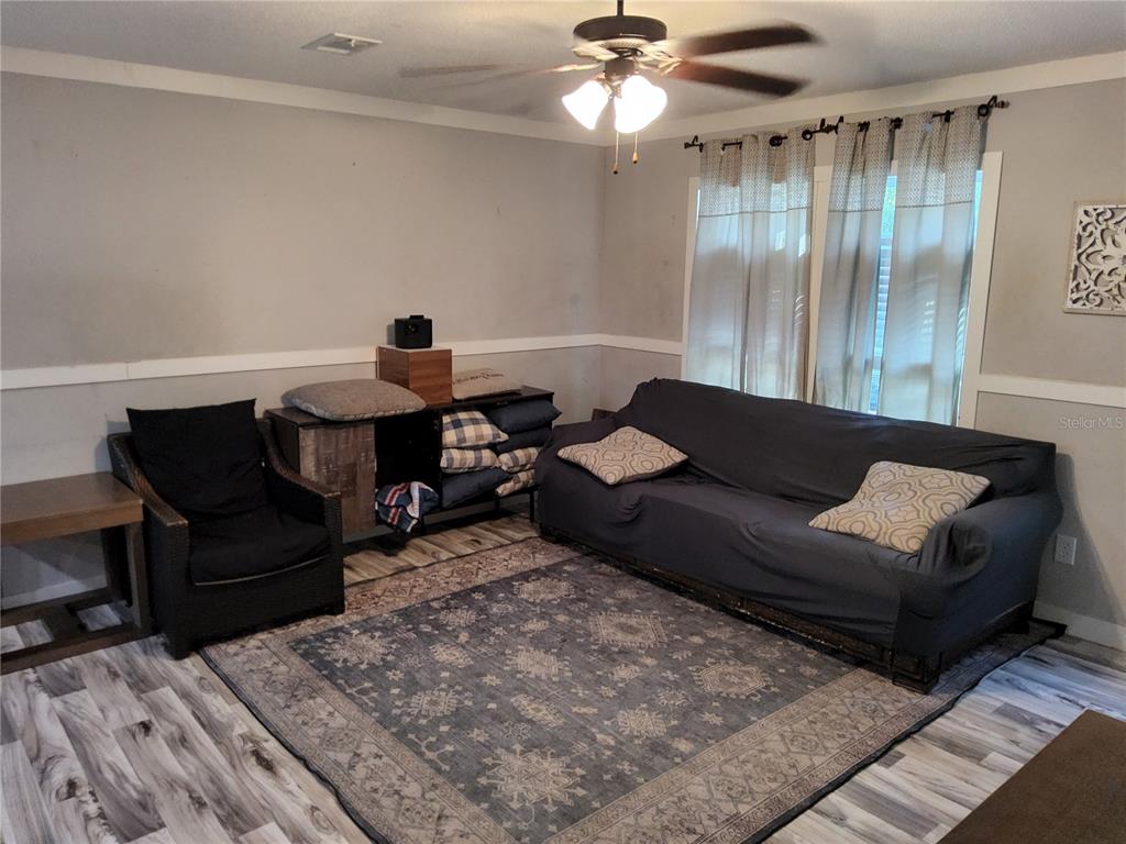 A living room features a dark sofa, an armchair, a patterned rug, and wood-look flooring — 3200 SE 107TH PLACE, OCALA, FL
