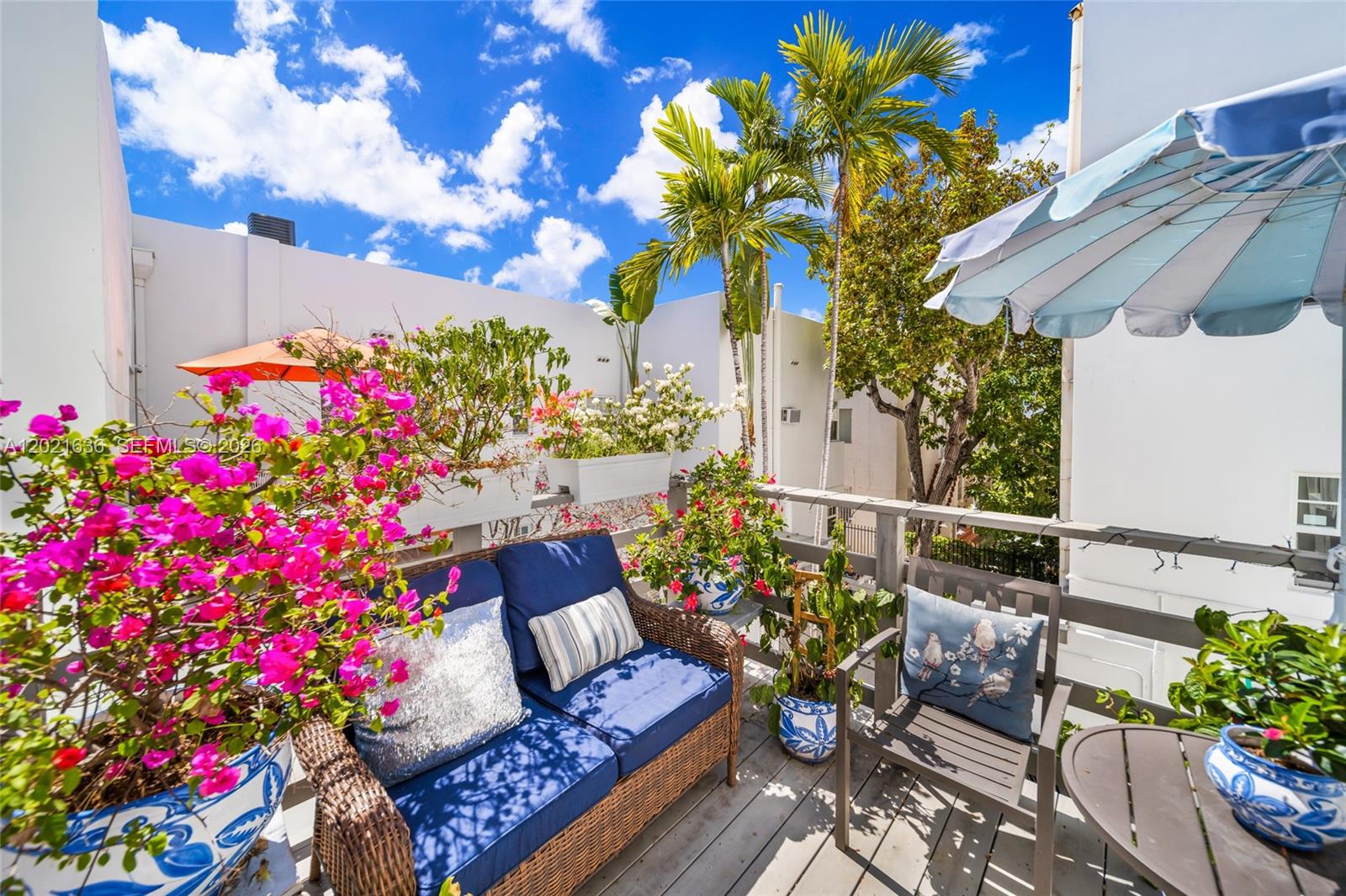 A sunny outdoor balcony features wicker seating, potted plants, and a blue-and-white striped umbrella — 408 W 25th St # 8, Miami Beach FL 33140, MIAMI BEACH, FL