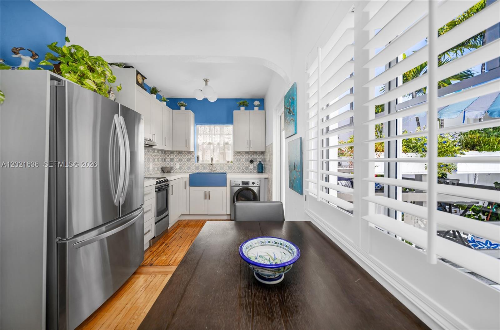 A kitchen features white cabinets, a blue farmhouse sink, stainless appliances, and a wooden table — 408 W 25th St # 8, Miami Beach FL 33140, MIAMI BEACH, FL