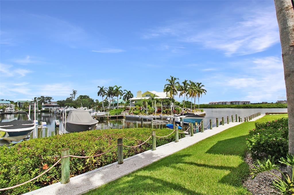 A waterfront view featuring a grassy lawn, a boat dock, and a house with palm trees — 1335 SIESTA BAYSIDE DRIVE UNIT 1335C, SARASOTA, FL