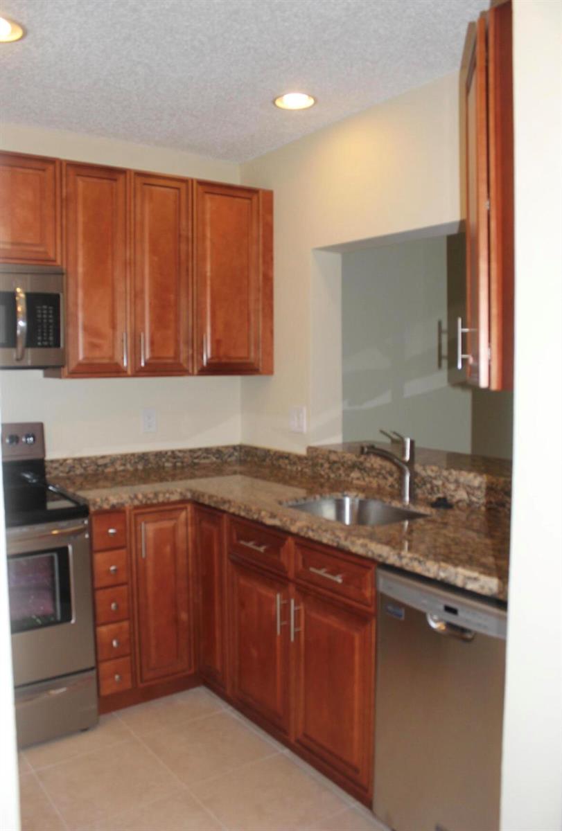 A kitchen features wood cabinets, granite countertops, stainless steel appliances, and a pass-through window — 21943 Remsen Terrace # 204, Boca Raton FL 33433, BOCA RATON, FL