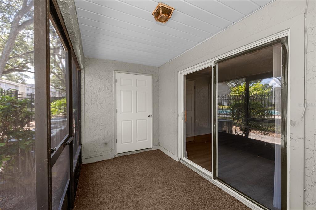 A screened-in patio with a brown carpeted floor, a white door, and sliding glass doors — 14424 REUTER STRASSE CIRCLE UNIT 104, TAMPA, FL