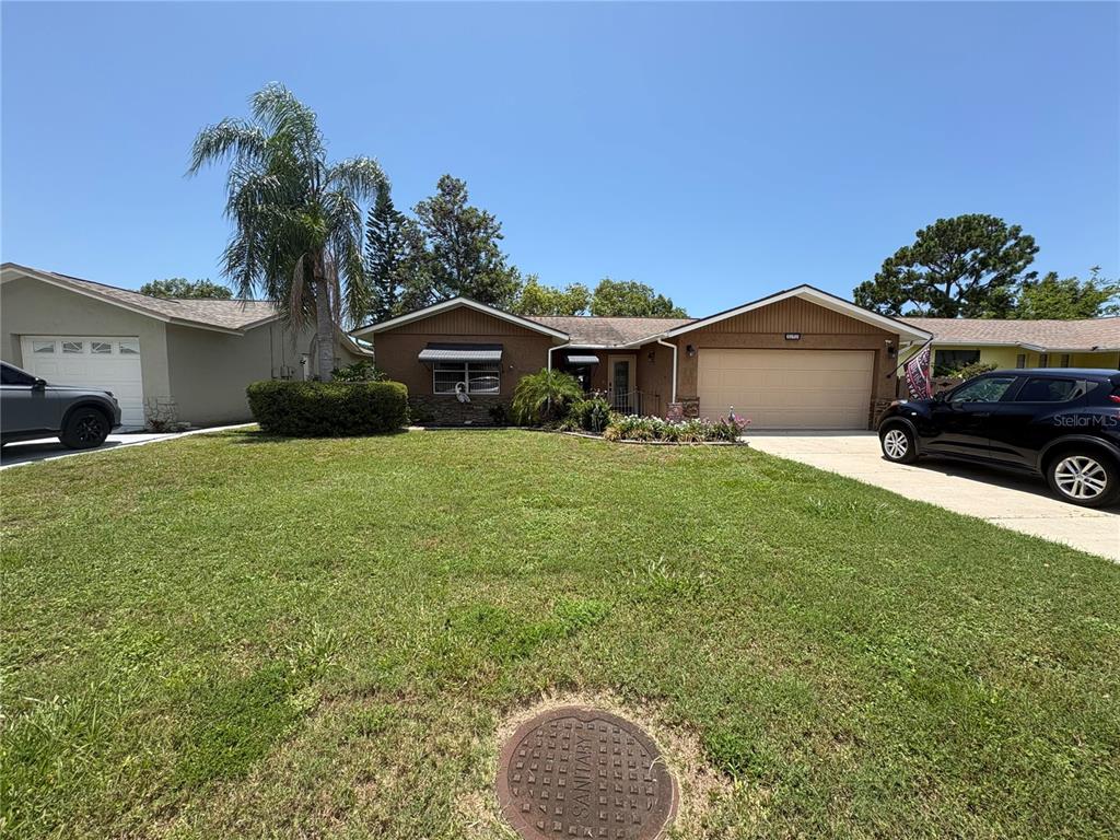 A tan single-story house features a two-car garage, a front garden, and a concrete driveway — 5049 SHERRY LANE, NEW PORT RICHEY, FL