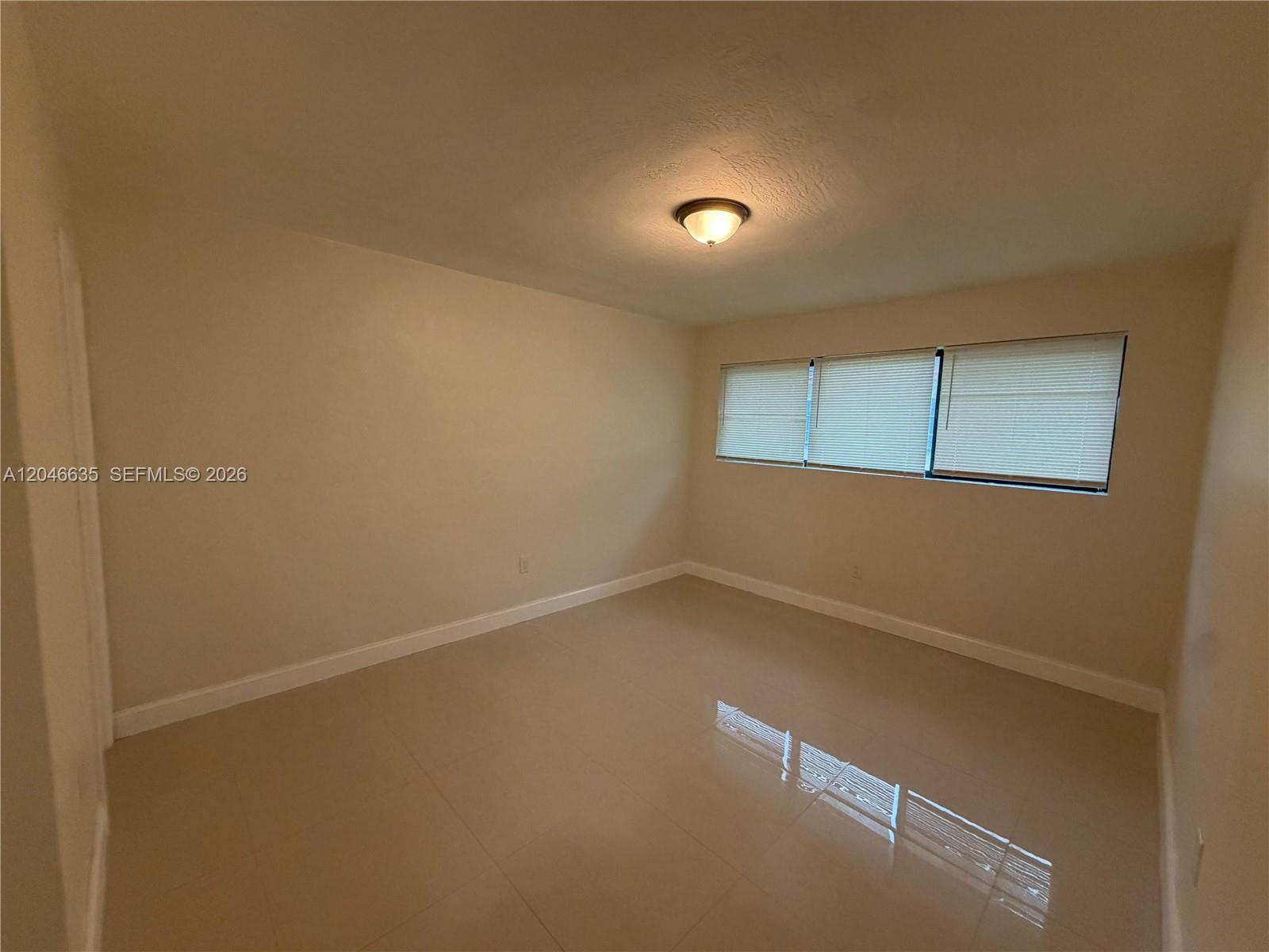 An empty room features beige walls, light-colored tile flooring, and three windows with blinds — NORTH MIAMI, FL