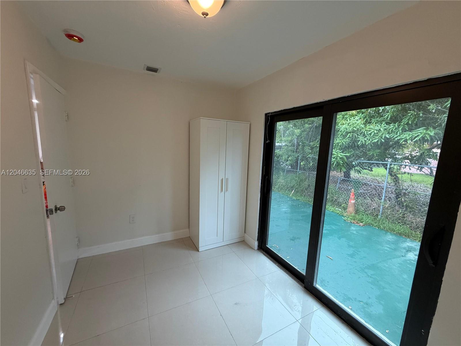 A small room with tiled floors, a white wardrobe, and a sliding glass door — NORTH MIAMI, FL