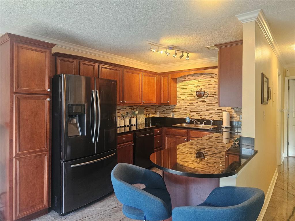 A kitchen with dark wood cabinets, black appliances, granite countertops, and two blue bar stools — 4882 CONWAY ROAD UNIT 82, ORLANDO, FL
