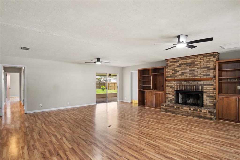 A living room features wood-look flooring, a brick fireplace, built-in shelving, and sliding glass doors — 2217 BOXWOOD WAY, BRANDON, FL