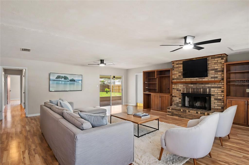 A living room features a brick fireplace, built-in wooden shelving, and light-colored wood flooring — 2217 BOXWOOD WAY, BRANDON, FL